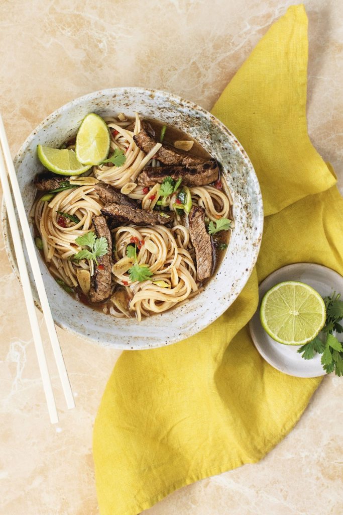 Slow Cooker Beef Pho with noodles, beef slices, and lime wedges in a bowl.