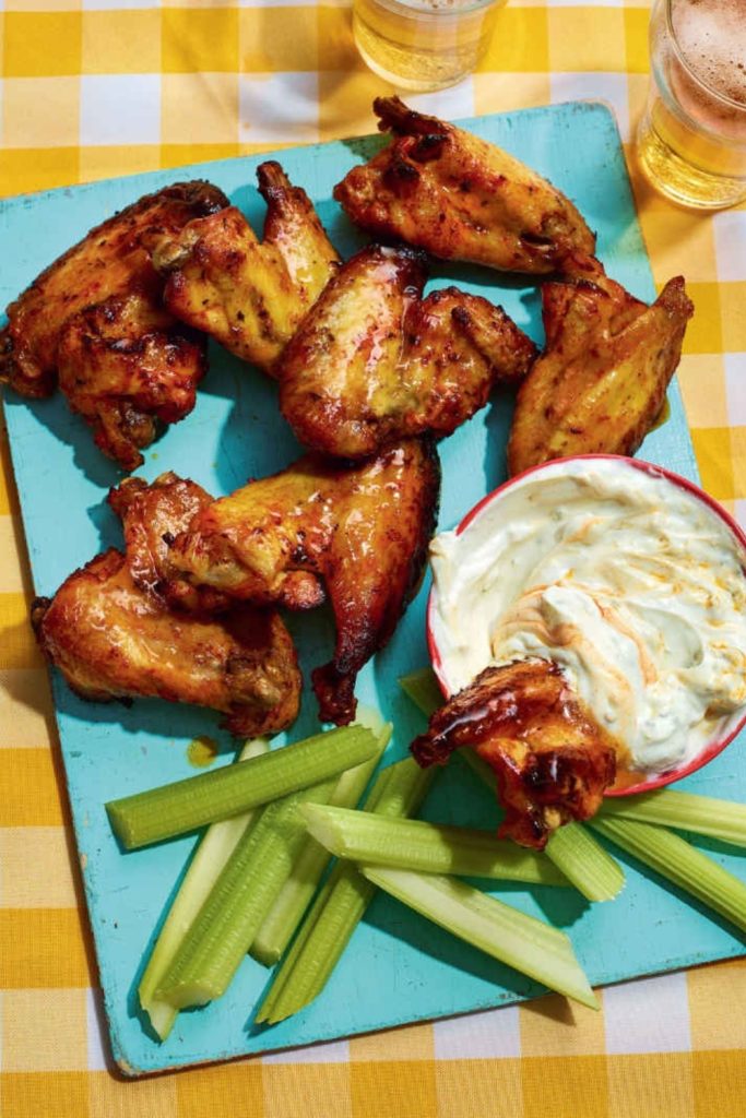 Buffalo chicken wings with celery sticks and dipping sauce on a turquoise board.