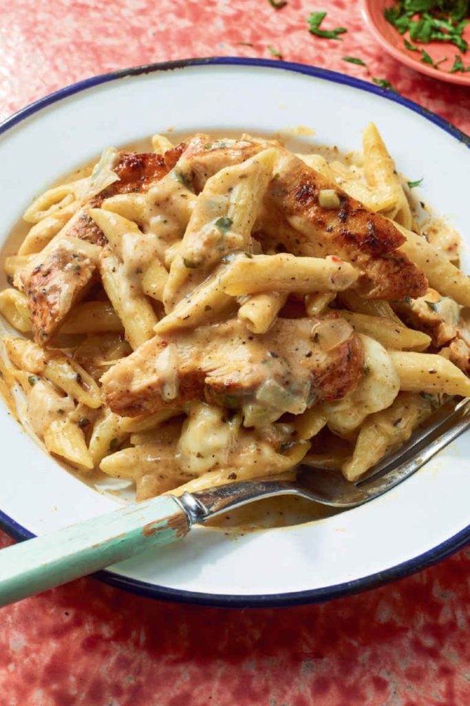 Slow Cooker Cajun Chicken and Penne Alfredo in a white bowl with a blue rim.