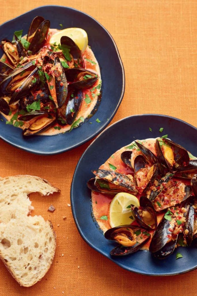 Slow Cooker Mussels in a tomato-based sauce with lemon wedges and parsley on a blue plate.