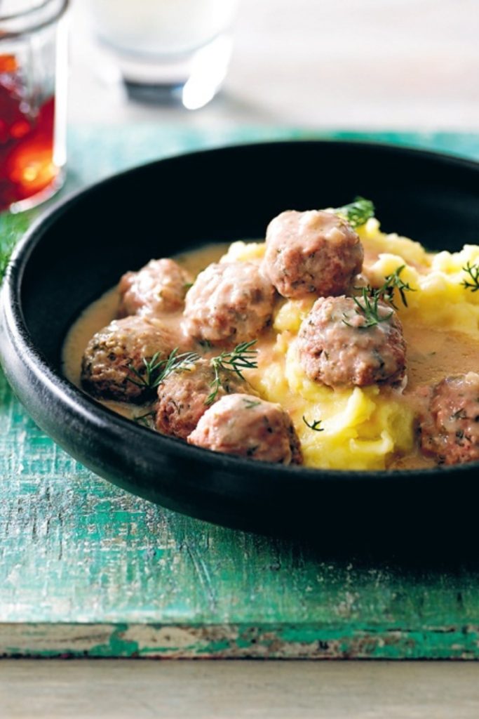 Slow Cooker Swedish Meatballs in creamy sauce, served over mashed potatoes in a black bowl, topped with dill.