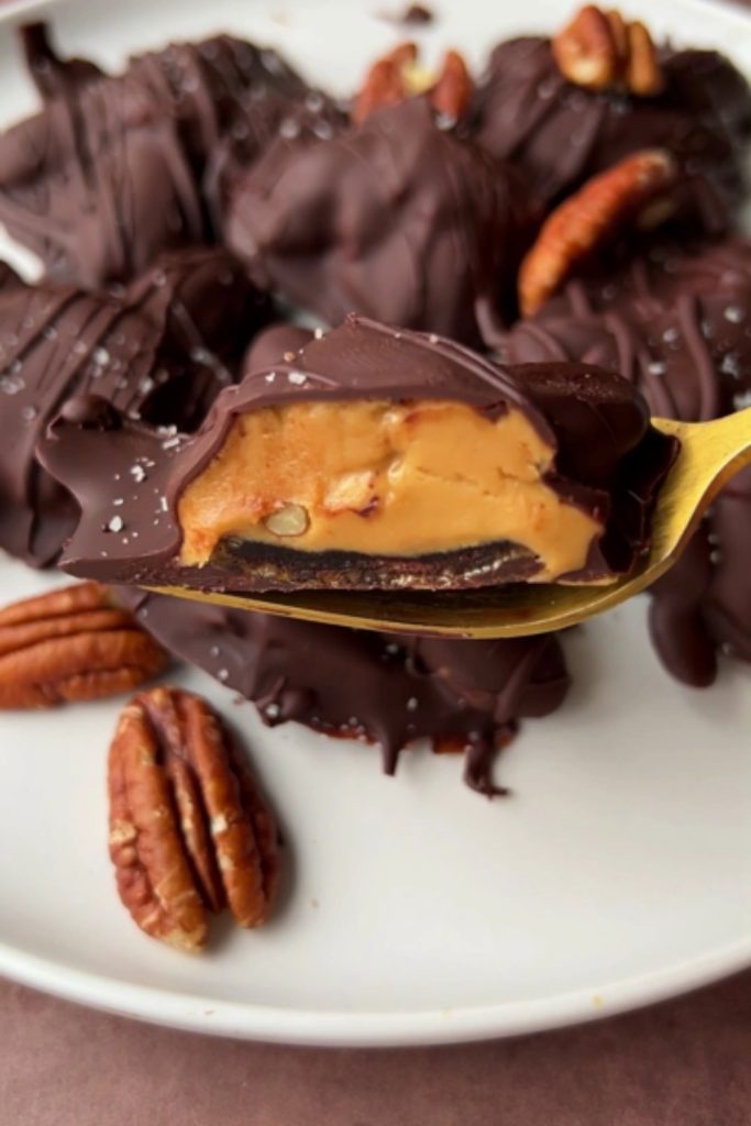 Slow Cooker Chocolate Turtle on a spoon, showing caramel and pecan filling, surrounded by more turtles.