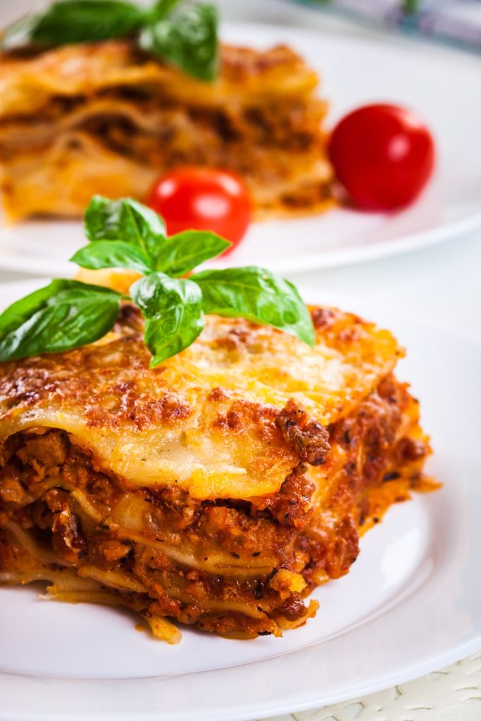 Slow Cooker Lasagna using Dolmio, garnished with basil and cherry tomatoes on a white plate.