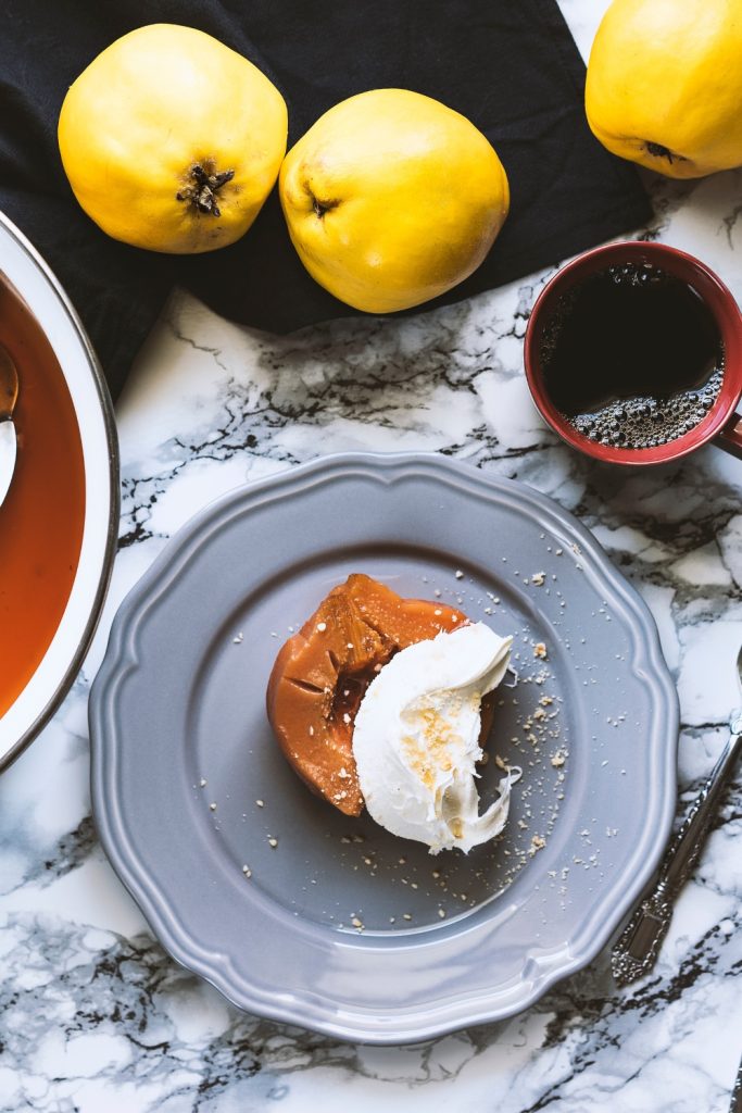 Poached Quince on a gray plate with whipped cream and whole quinces.
