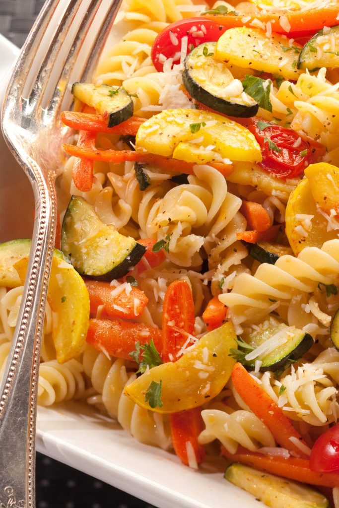 Slow cooker pasta primavera with zucchini, carrots, and tomatoes, sprinkled with cheese.