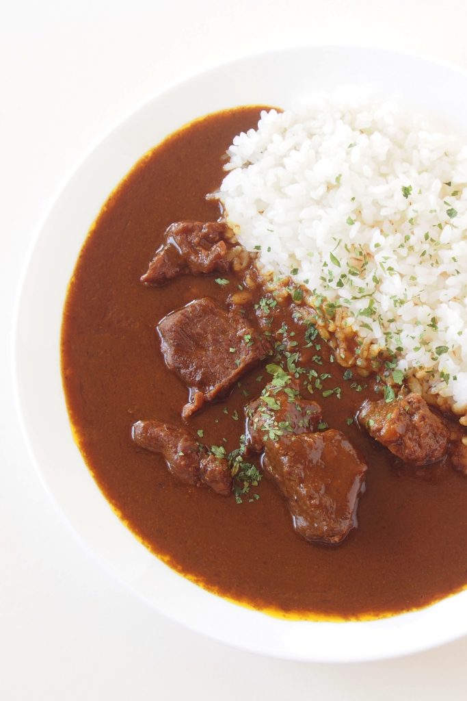 Slow-cooked kangaroo curry served with rice on a white plate, garnished with parsley.