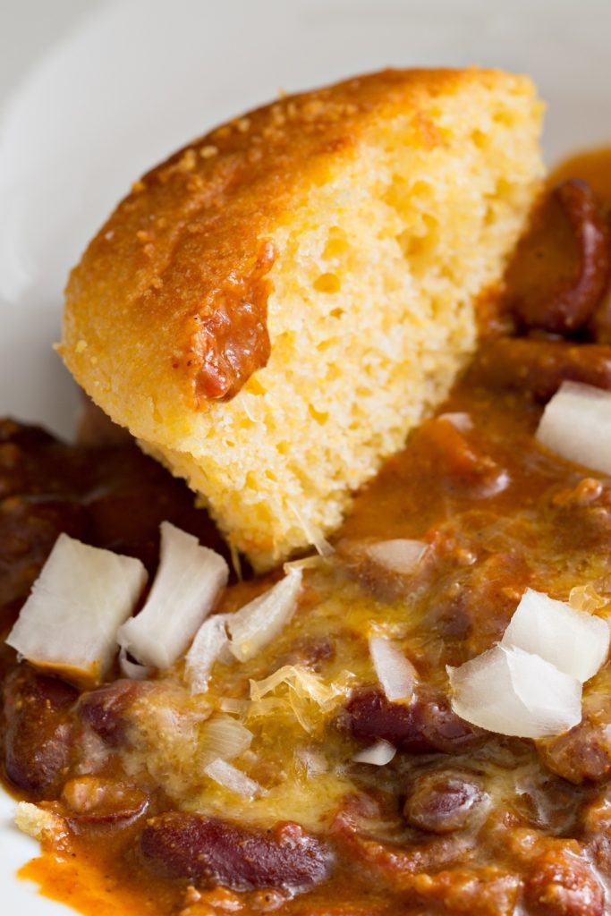 A piece of Jiffy cornbread served with chili and chopped onions.