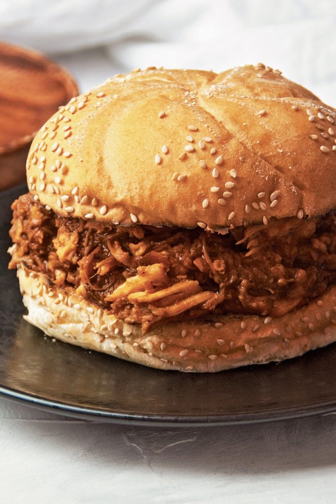 Slow Cooker BBQ Pulled Pork sandwich with a sesame seed bun, served on a black plate.