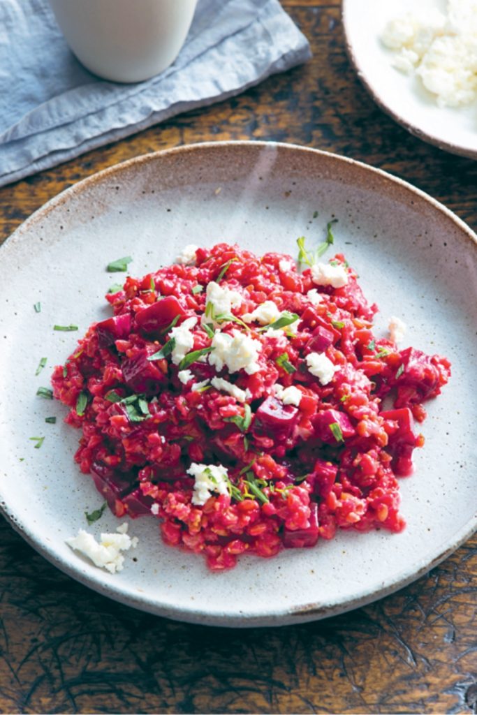Slow Cooker Beetroot Risotto with crumbled cheese and herbs on a plate, with a drink cup.