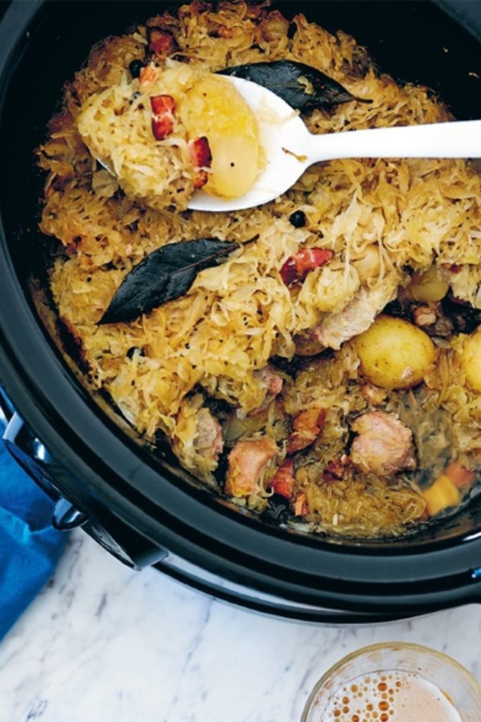 Slow Cooker Choucroute with sauerkraut, potatoes, and sausages being served from the slow cooker.