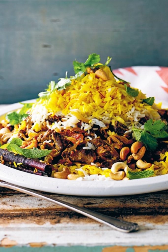 Slow Cooker Lamb Biryani served on a white plate with yellow and white rice, garnished with cilantro and cashews.