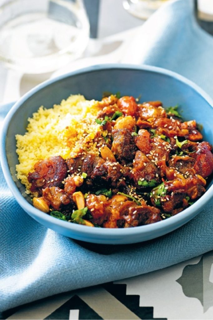 Slow Cooker Lamb Tagine Harissa served in a blue bowl with couscous, garnished with sesame seeds.