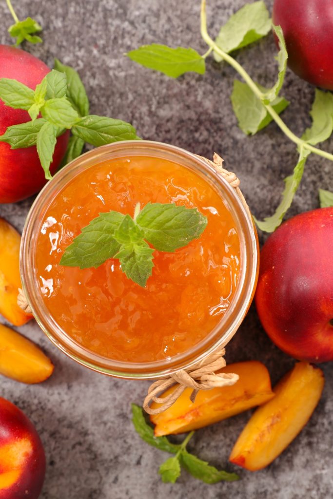 Slow Cooker Peach Jam Preserves in a jar, garnished with mint, surrounded by fresh peaches.