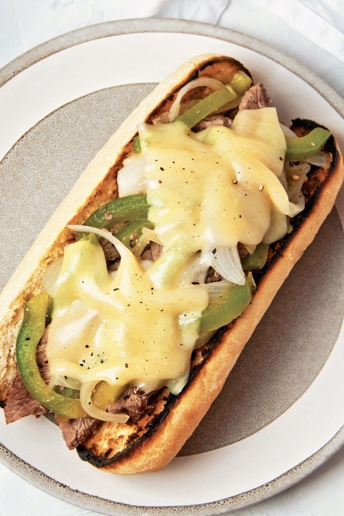 Slow Cooker Philly Cheesesteak with melted cheese, green peppers, and onions on a toasted roll.