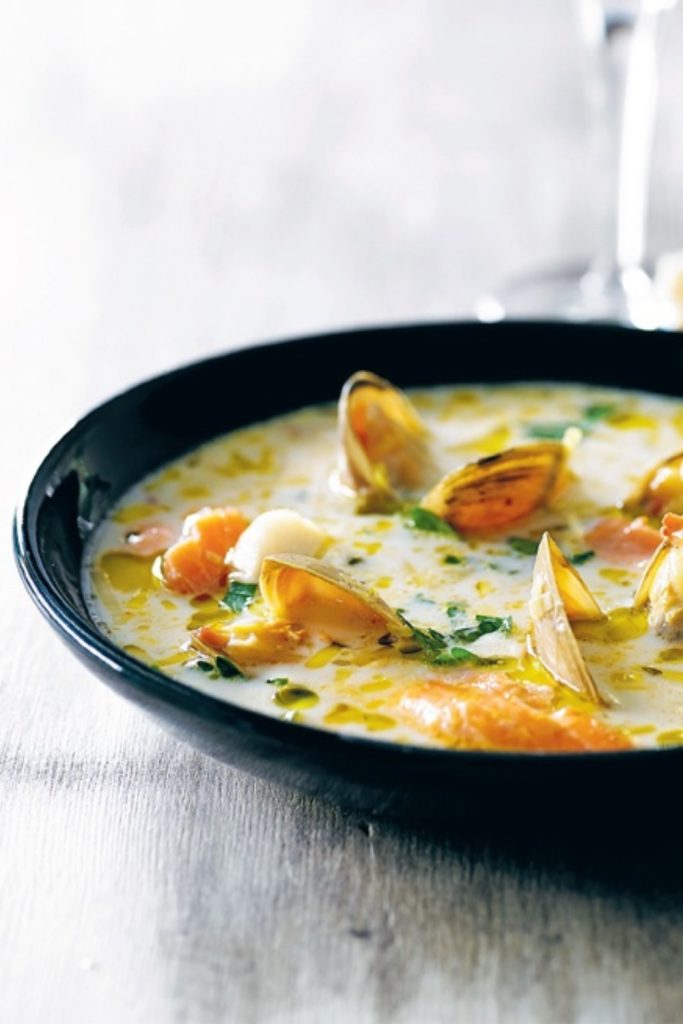 Seafood Chowder in a black bowl with clams and fish in a creamy broth.