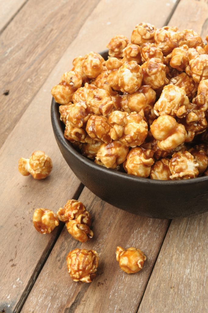 Caramel-coated popcorn in a black bowl on a wooden table.