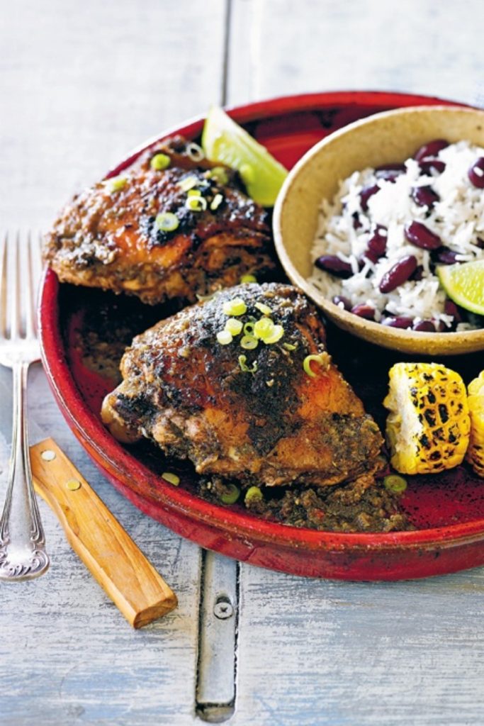 Slow Cooker Jerk Chicken served with grilled corn and rice with beans on a red plate.
