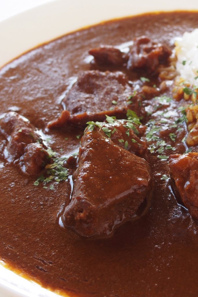Slow-cooked kangaroo curry with tender meat pieces and rich sauce garnished with parsley.