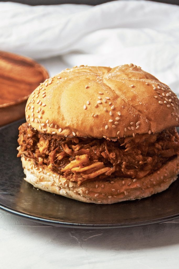Slow Cooker BBQ Pulled Pork sandwich on a sesame seed bun, served on a black plate.
