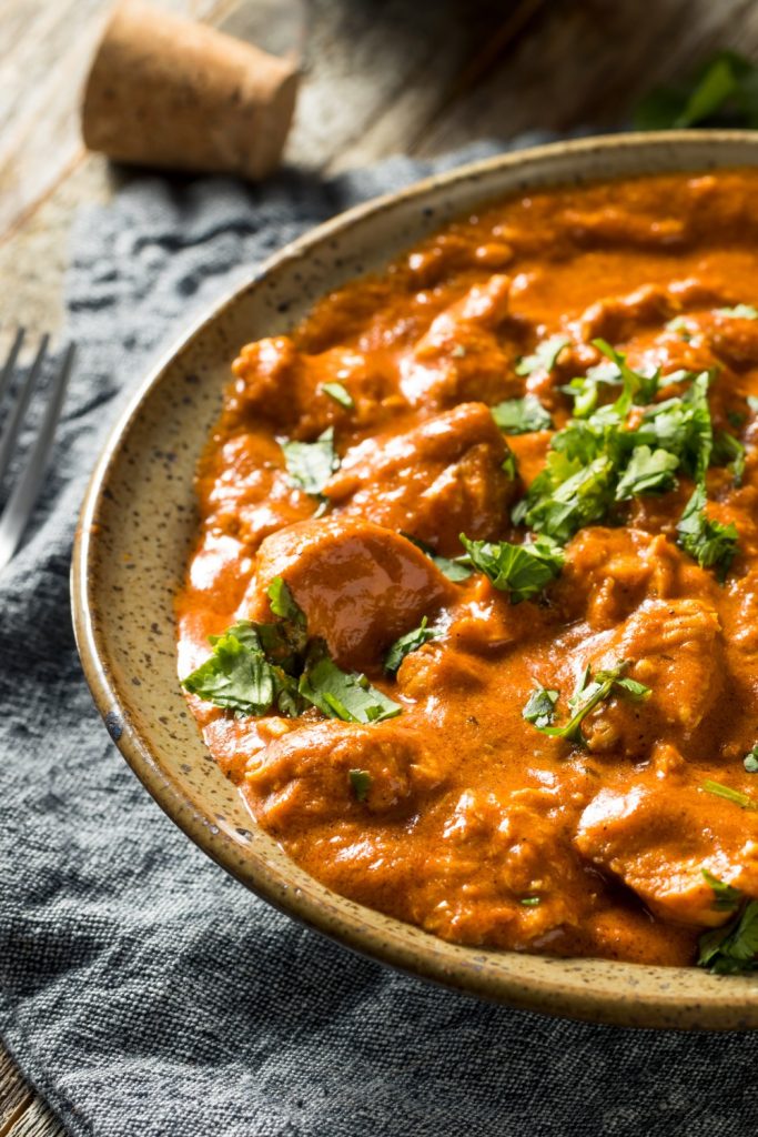 Slow Cooker Butter Chicken with rich sauce, garnished with cilantro in a brown ceramic bowl.
