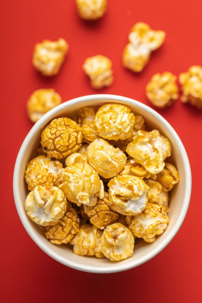 Caramel-coated popcorn in a white bowl on a red background.
