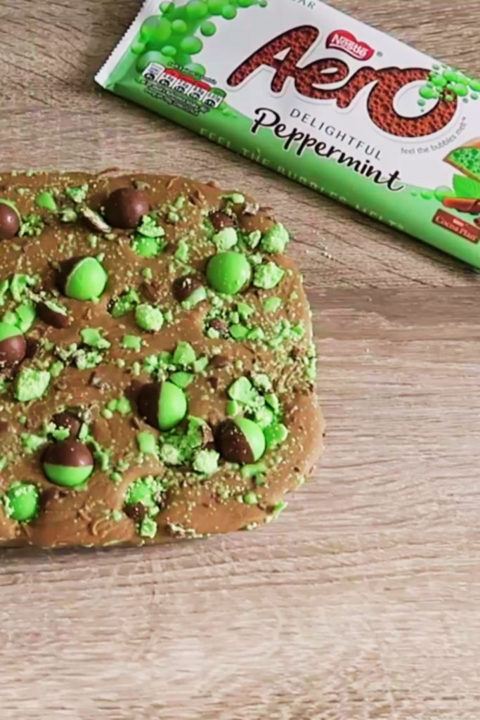 Slow Cooker Mint Aero Fudge topped with green Aero pieces on a wooden surface.