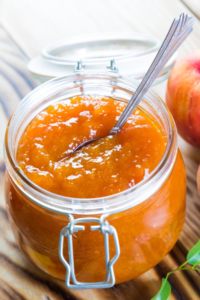 Slow Cooker Peach Jam Preserves in a glass jar with a spoon.