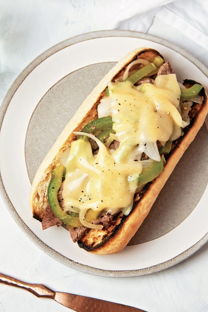 Slow Cooker Philly Cheesesteak on a toasted roll with melted cheese, green peppers, and onions.