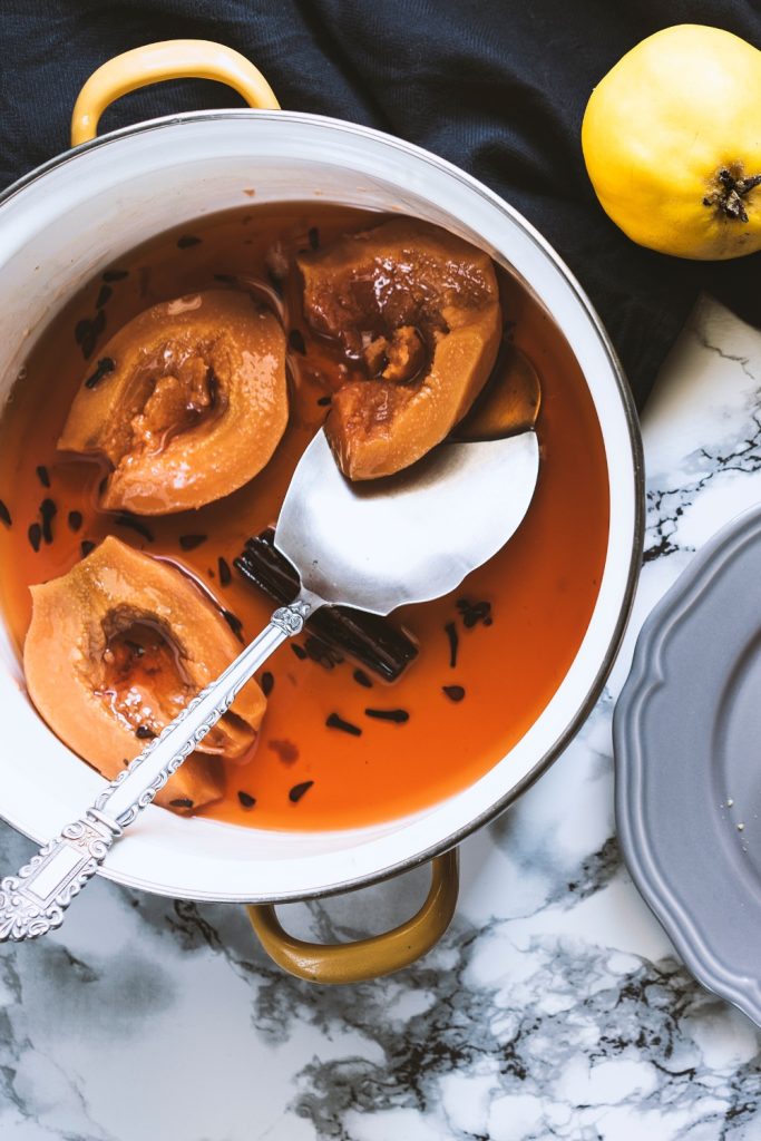 Slow Cooker Poached Quince halves in a pot with syrup and spices.