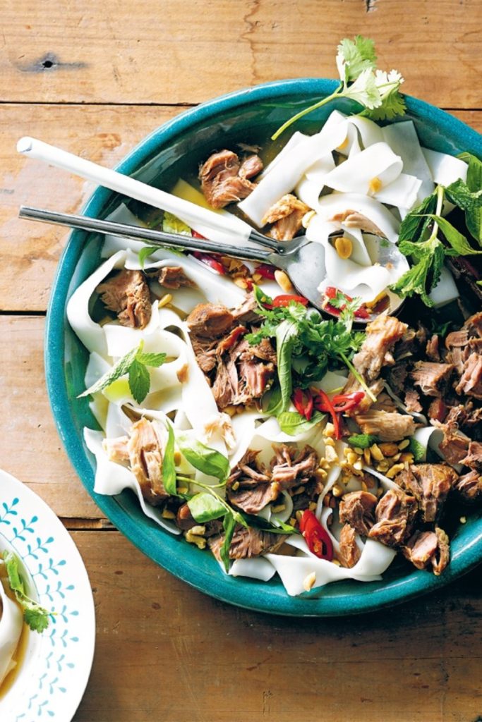 Slow Cooker Pork Cheeks with rice noodles, fresh herbs, and sliced chilies in a green bowl.