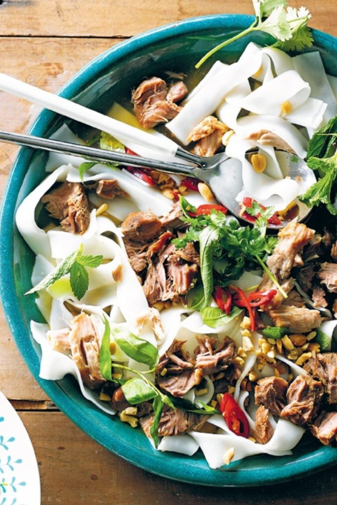 Slow Cooker Pork Cheeks with rice noodles, fresh herbs, and peanuts in a green bowl.