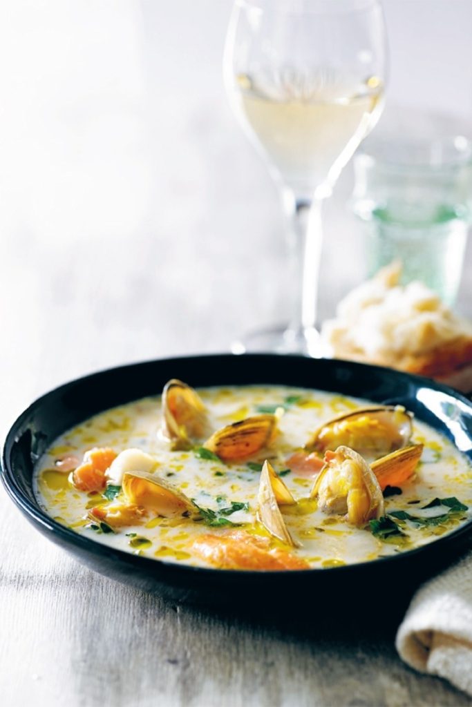 Slow Cooker Seafood Chowder served in a black bowl with clams, fish, and a creamy broth.