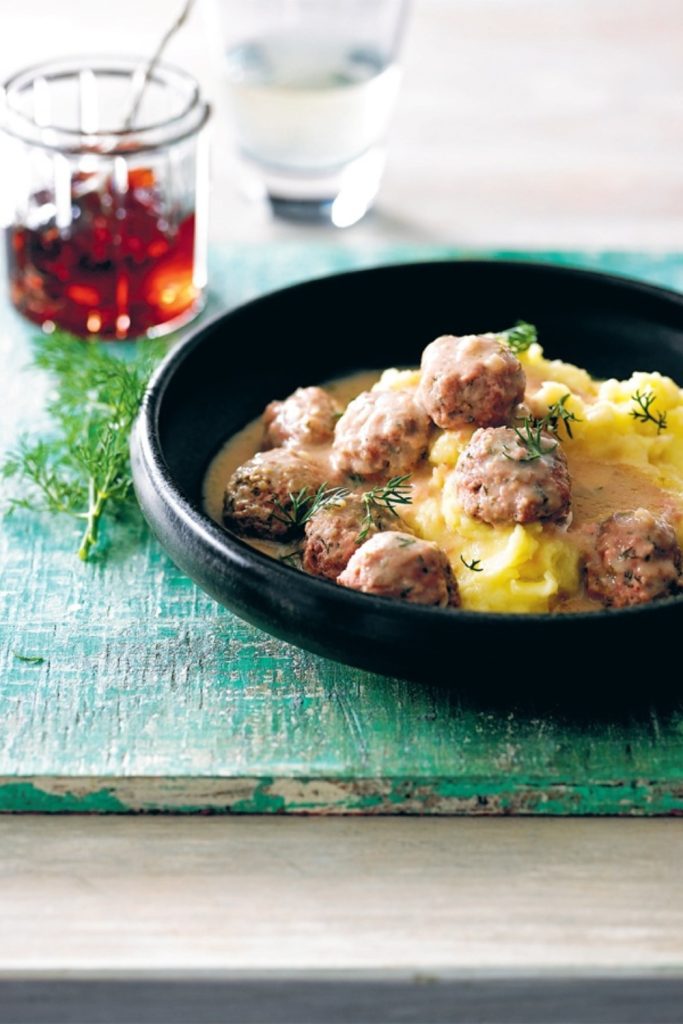 Slow Cooker Swedish Meatballs with creamy sauce and mashed potatoes in a black bowl, garnished with dill.