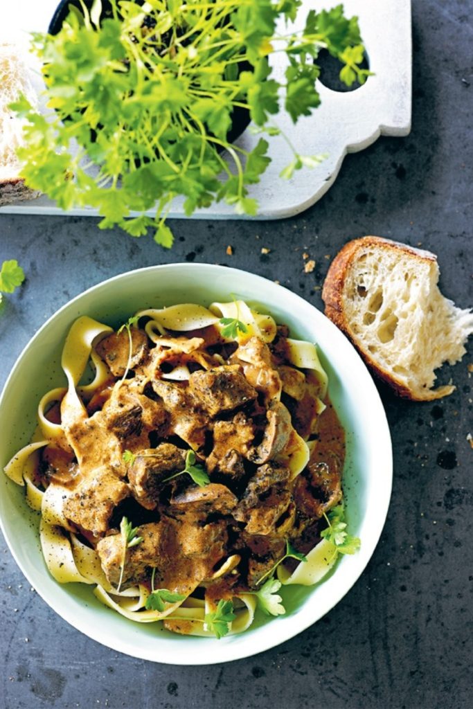 Veal Stroganoff in Slow Cooker served over pasta with bread on the side.