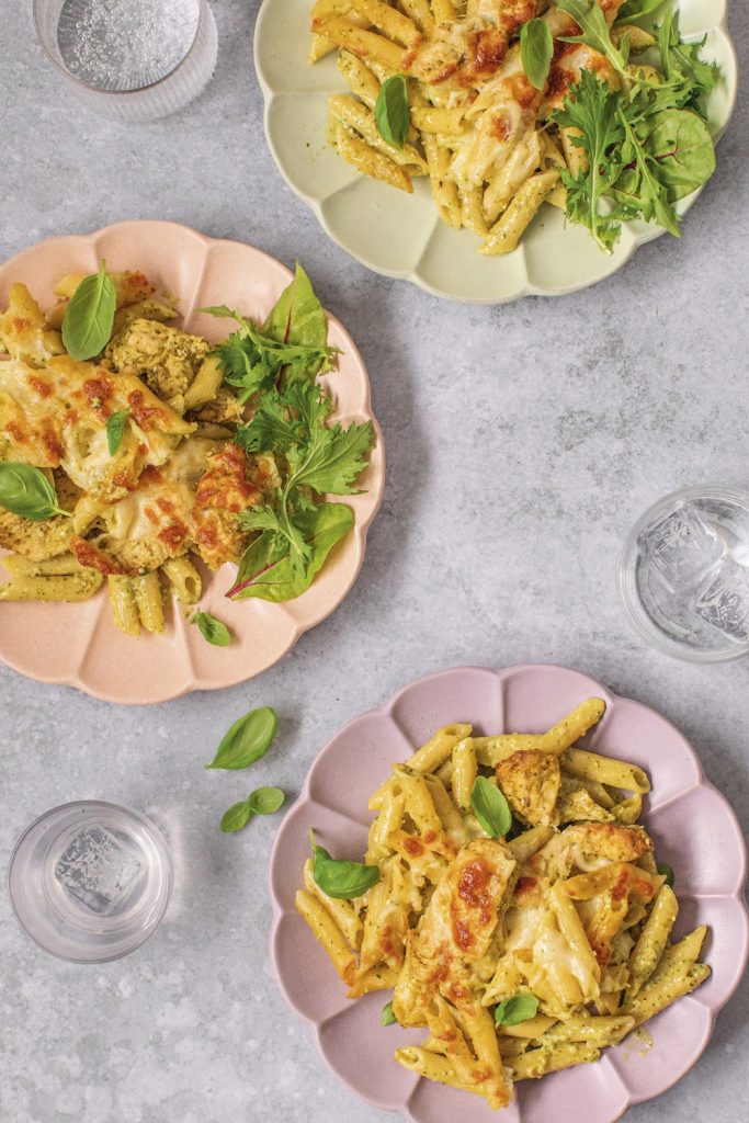 Plates of slow cooker chicken pesto pasta with fresh greens on colorful plates.