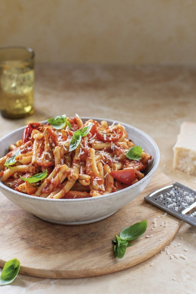 Bored of Lunch Slow Cooker Pasta Arrabbiata in a white bowl with basil and cheese on a wooden board.