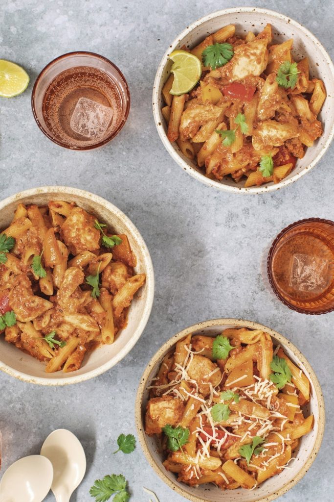 Bored of Lunch Slow Cooker Tex Mex Chicken Pasta served in three bowls with lime and drinks on the side.