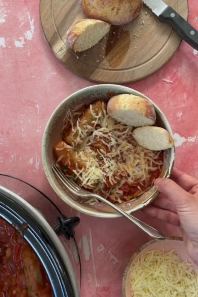 Sausage and baked bean casserole in a bowl topped with cheese, served with bread.