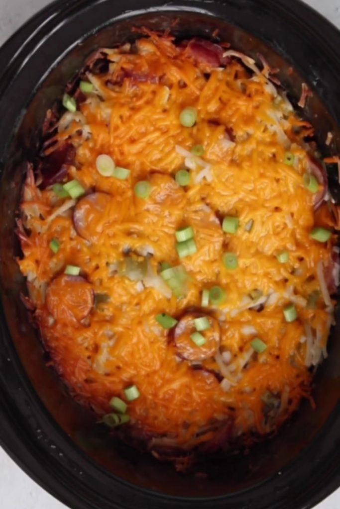 Serving of Cheesy Kielbasa Hashbrown Casserole on a spoon with green onions.