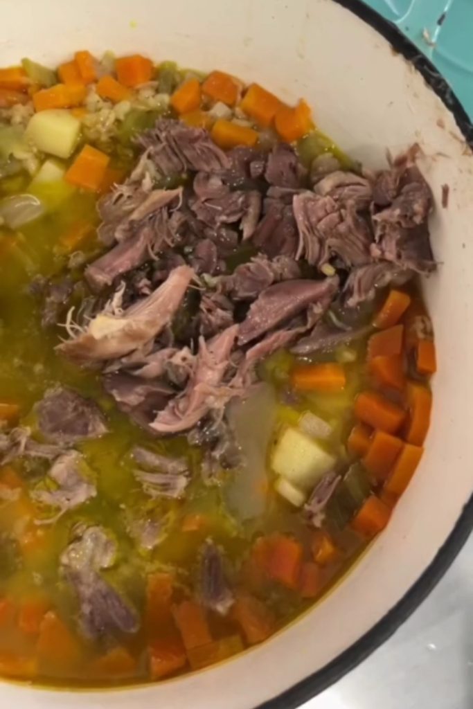 A pot of Slow Cooker Lamb Shank Soup with lamb, carrots, celery, and barley.