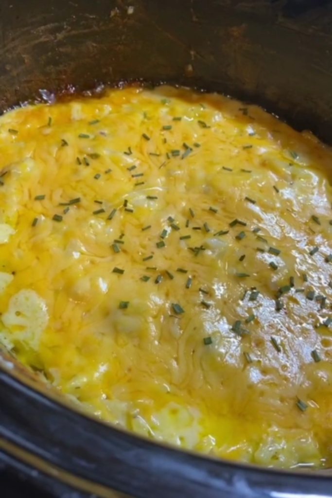 Cracker Barrel Hashbrown Casserole being served from a slow cooker with melted cheese on top.