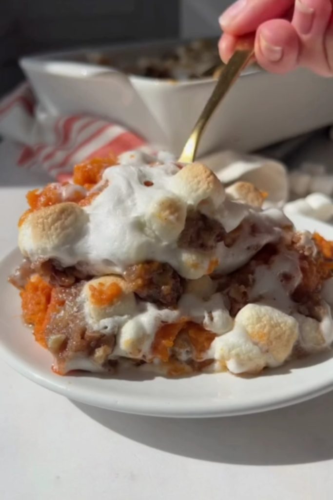 A serving of Sweet Potato Casserole with marshmallows and pecans on a white plate.