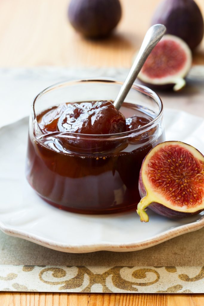 Jar of fig and ginger jam with fresh figs on a plate.