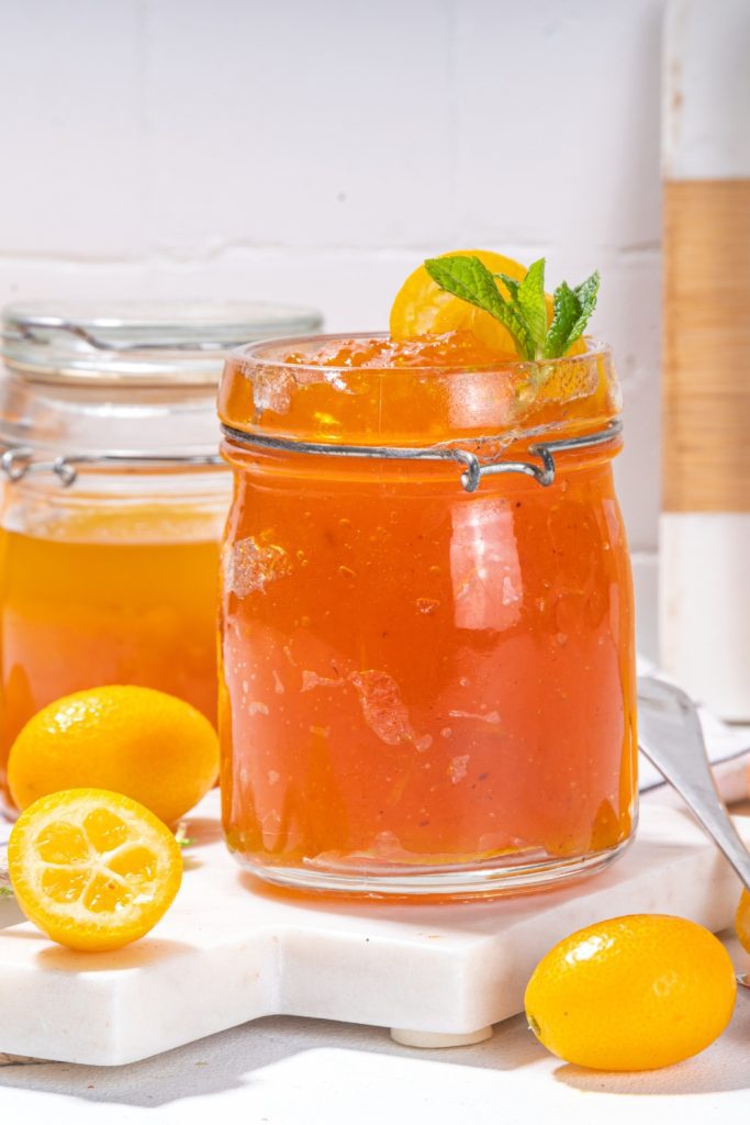 Jar of kumquat jam with mint leaves and fresh kumquats around.