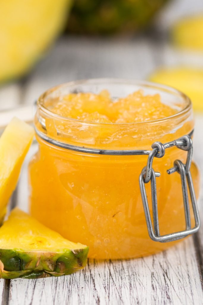 Bowl of pineapple jam with fresh pineapple slices on a rustic surface.