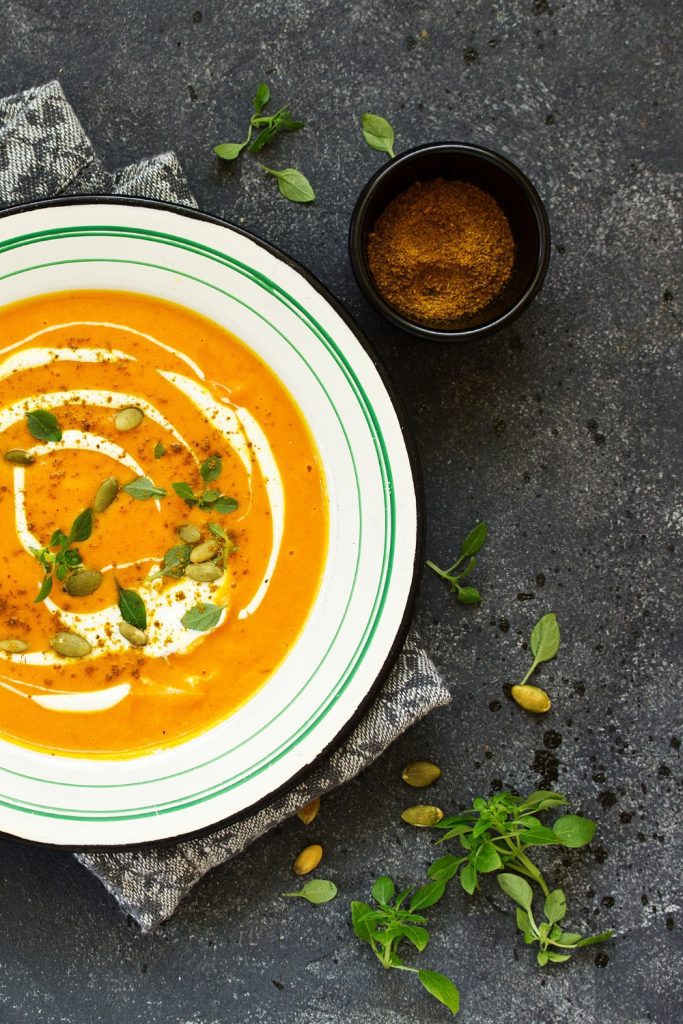 4-ingredient Slow Cooker Pumpkin Soup with a spoon, cream, and herbs.