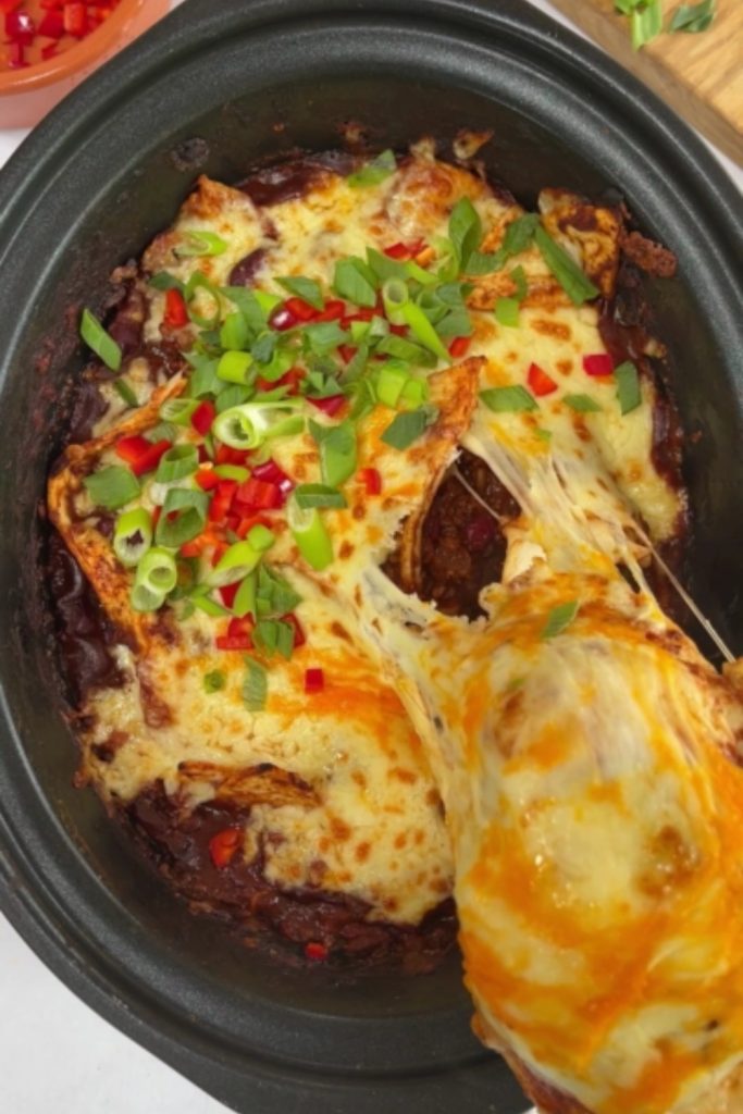 Beef Enchilada Casserole in a slow cooker with a serving spoon and fresh toppings.