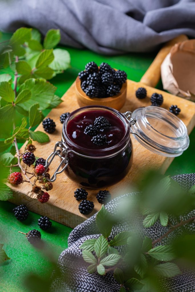 Jar of blackberry Apple jam with fresh blackberries on a wooden board.