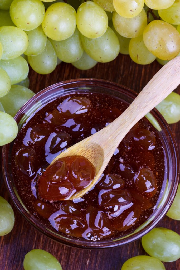 Slow Cooker Grape Jam in a bowl with a wooden spoon and fresh grapes.