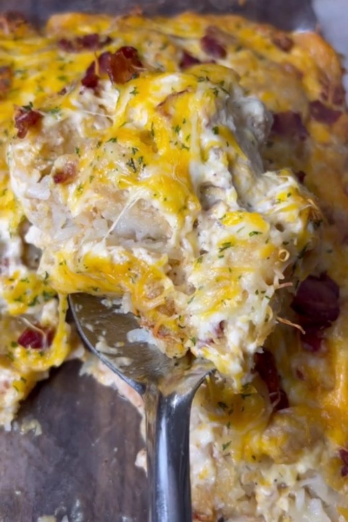 A serving spoon scooping out Tater Tot Chicken Casserole with cheese and bacon.